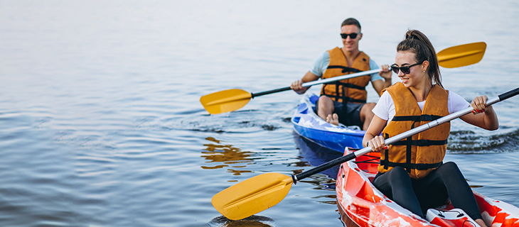 na imagem, vemos um homem e uma mulher a bordo de um bote, vestindo coletes de segurança na cor amarela, navegando em mar aberto.