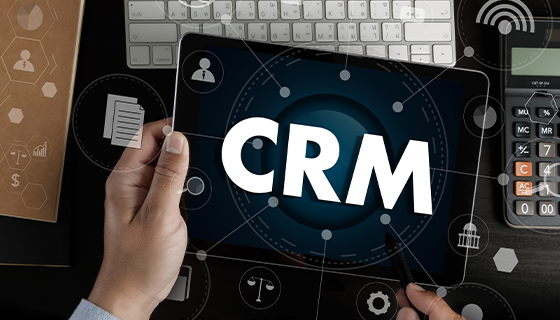 na imagem, vemos uma pessoa segurando um tablet com a sigla CRM escrito na tela, representando o CRM para turismo.